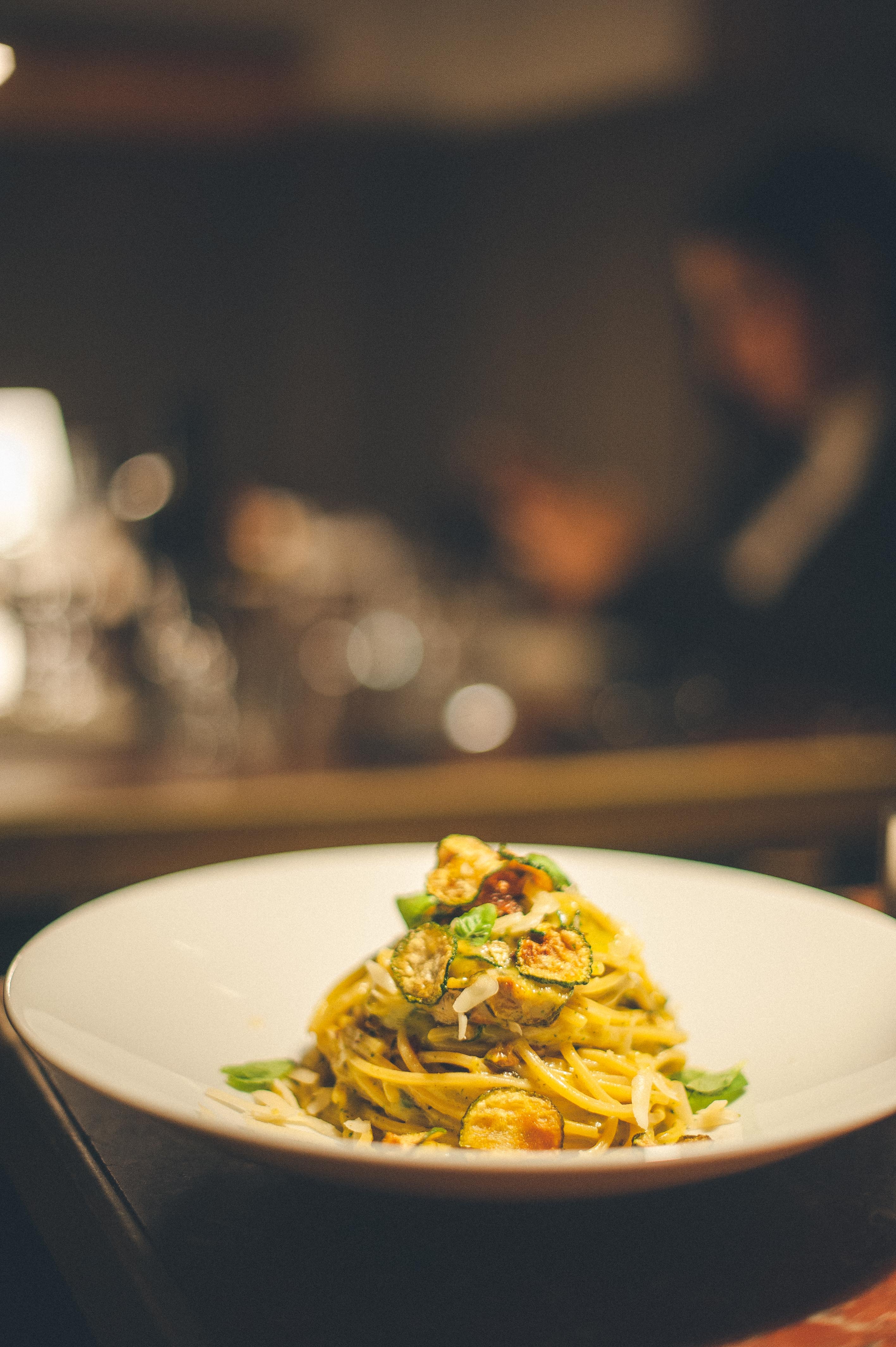 Piatto fondo bianco con un nido di pasta lunga condita, servito in sala con luci calde