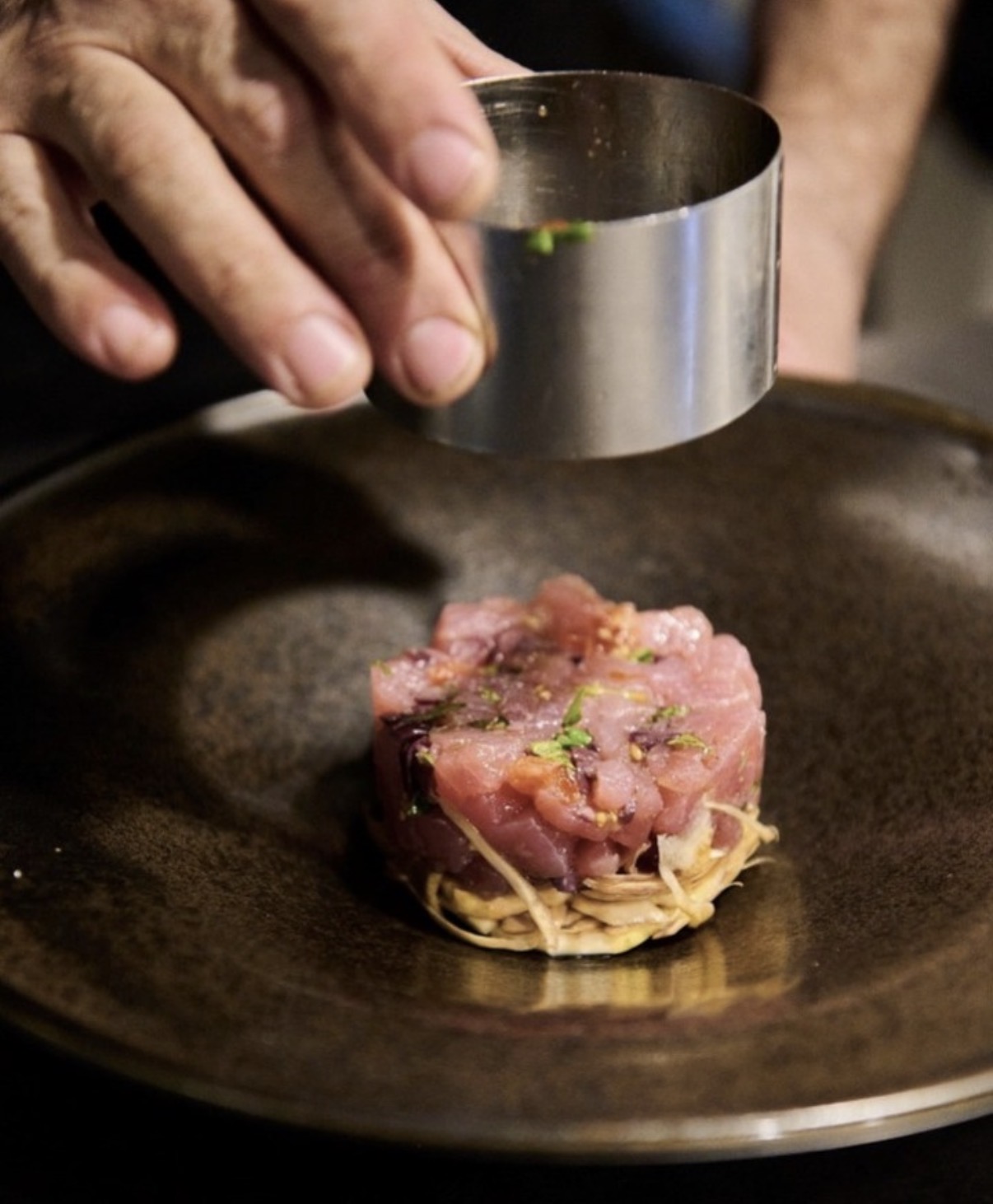 Mano che solleva un coppapasta metallico da un piatto scuro dopo l'impiattamento