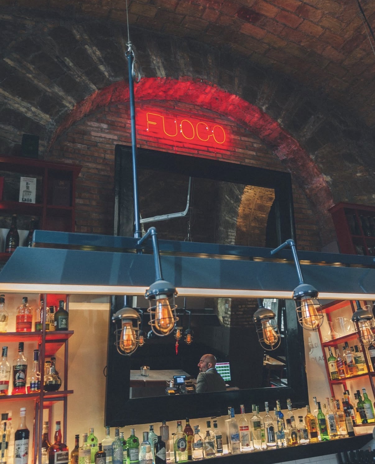 Insegna al neon rossa FUOCO sopra il bancone bar tra bottiglie e lampadine a vista